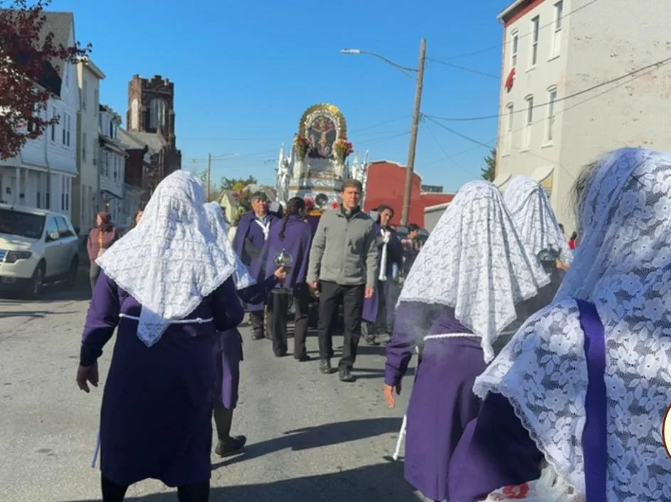 Parishioners in purple with white lace mantillas walk in Hispanic Catholic procession behind a baroque shrine through the streets of Allison Hill.