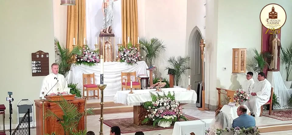 The sanctuary at St. Francis during Easter — altar with white lilies, the Alleluia banner, and clergy in white vestments.